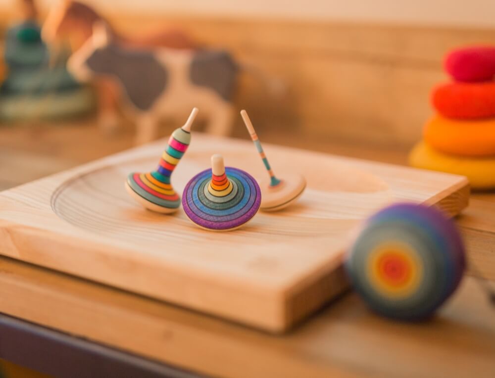 Three Mader rainbow spinning tops on a wooden spinning plate with a handcrafted yoyo alongside them