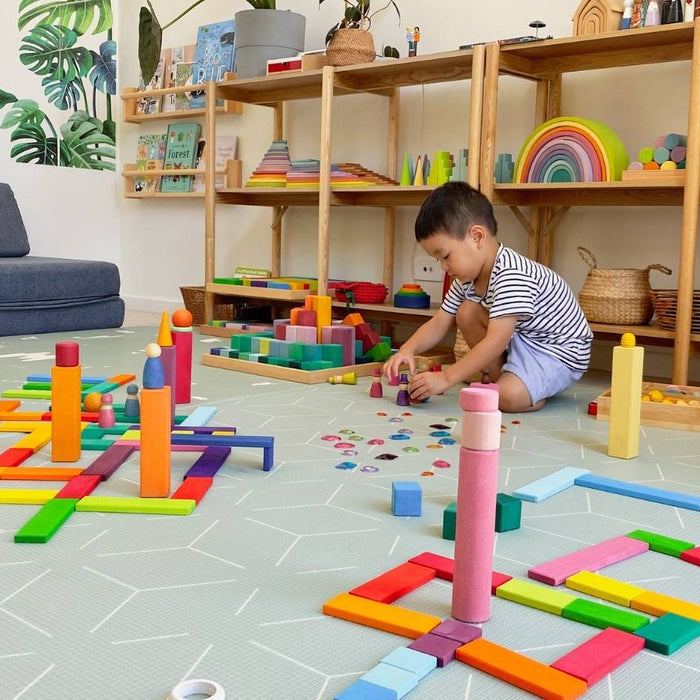 Two children playing with colourful building blocks on a play mat in a room with shelves of open-ended toys