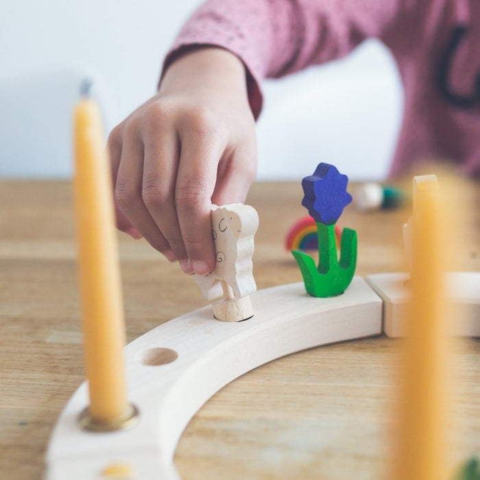 Child building a Grimm's Celebration Ring table centrepiece with candles and colourful celebration figures