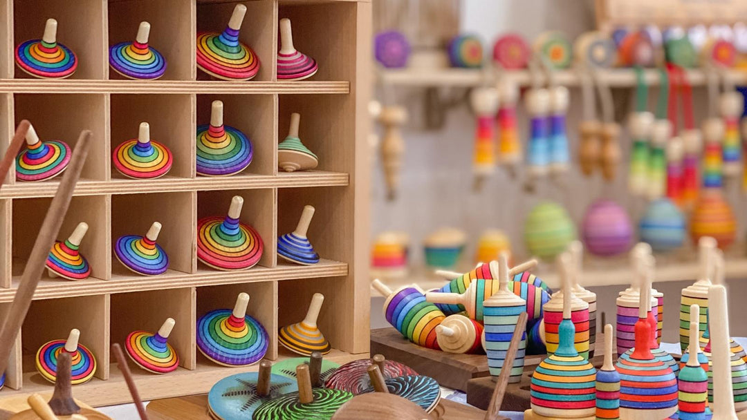 A store display of colourful Mader handcrafted wooden spinning tops, with skipping ropes and yo-yos in the background