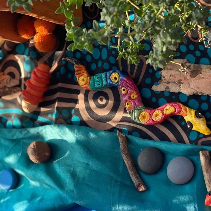 A child playing with a finished serpent-themed nature artwork for NAIDOC Week