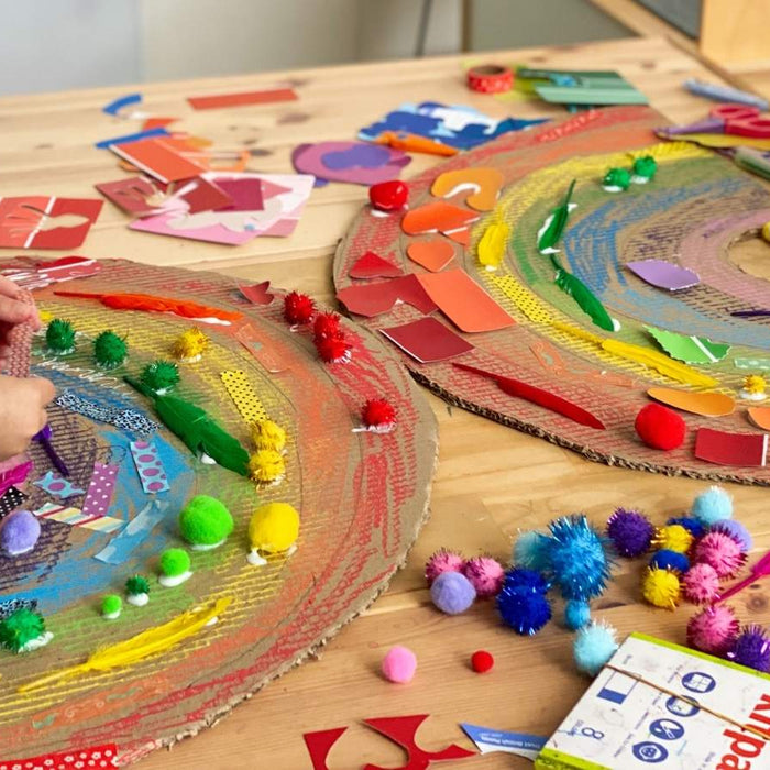 Children crafting colourful rainbows using Kitpas crayons, recycled cardboard and collage materials. One child is visible on the left and another is visible on the right, working on the projects.