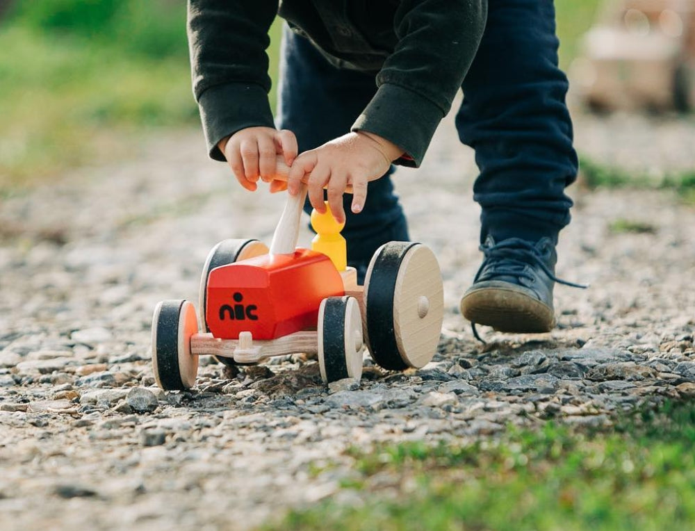 Child playing with a nic wooden toy vehicle outdoors