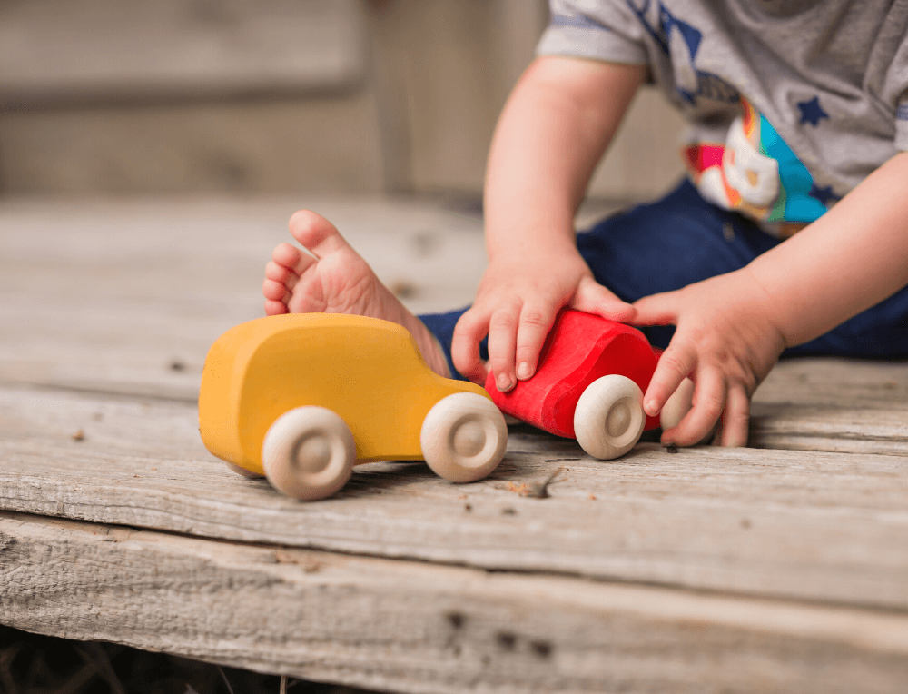 Toddler playing with Grimm's wooden cars in red and yellow