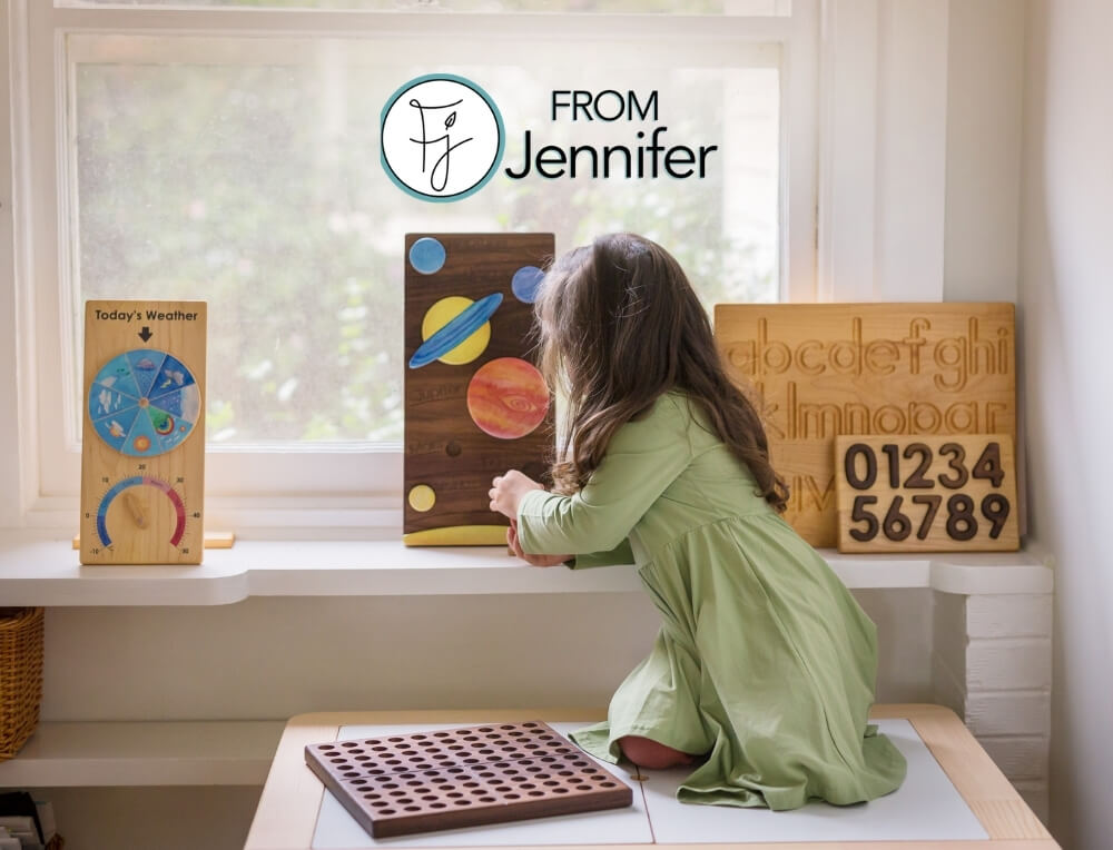 From Jennifer lifestyle image with logo, featuring a child interacting with a wooden educational toy. On the windowsill are other wooden learning toys, including a planet board. weather chart and an alphabet/number board – Oskar's Wooden Ark