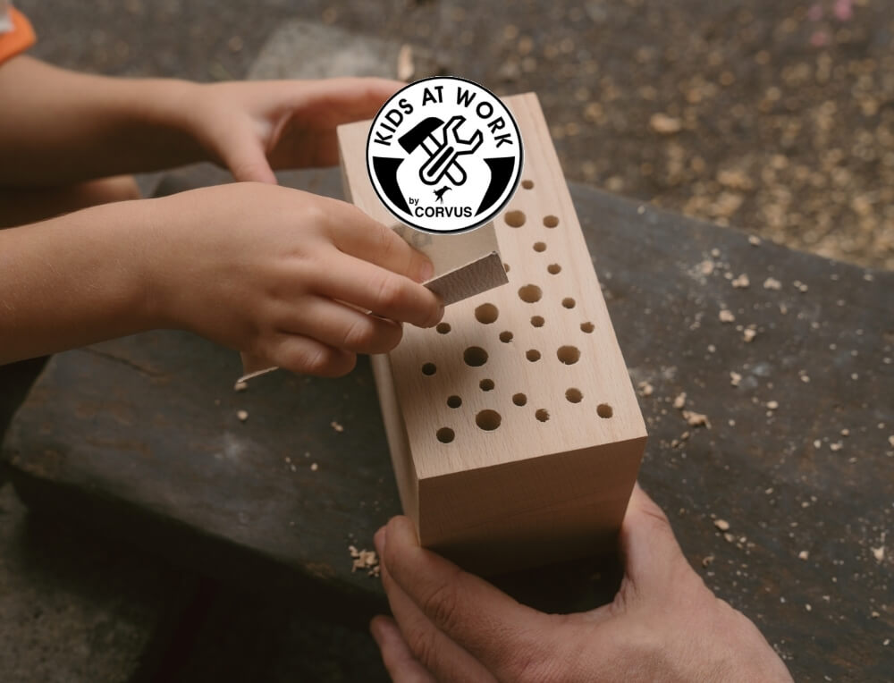 Kids at Work by Corvus lifestyle image with logo, featuring a child's hands  using sandpaper to smooth the edge of a wooden bug hotel – Oskar's Wooden Ark