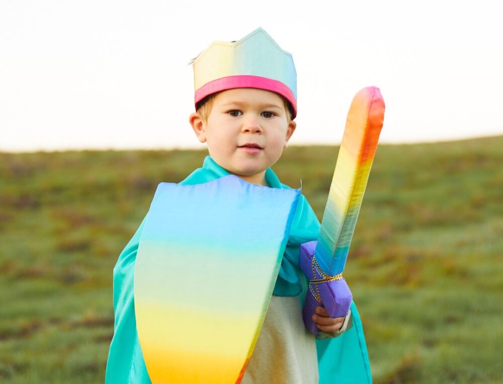 Boy engaging in heroic pretend play outdoors, dressed in Sarah's Silks Rainbow Crown, Sword, Shield, and Play Silk