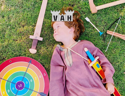 VAH historical role play lifestyle image with logo, featuring a child dressed in robes, surrounded by a toy sword, crossbow and target  – Oskar's Wooden Ark