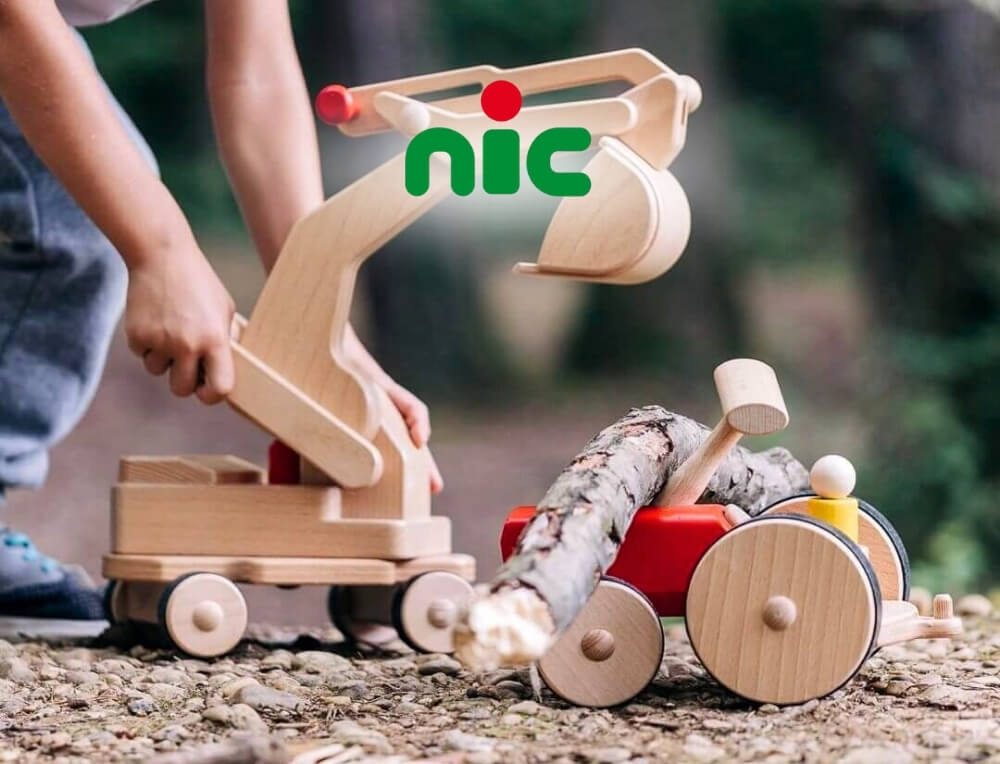 nic Wooden Toys lifestyle image with logo, featuring a child's hands pushing a wooden toy excavator and tractor outdoors on a gravel path – Oskar's Wooden Ark