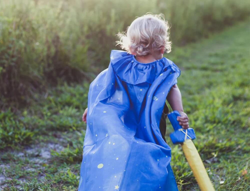 Child wearing a silk cape and holding a toy sword in an outdoor setting - discontinued products on sale at Oskar's Wooden Ark