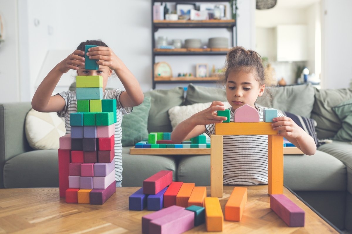 Two children playing with colourful Grimm's building blocks on a table in a living room.