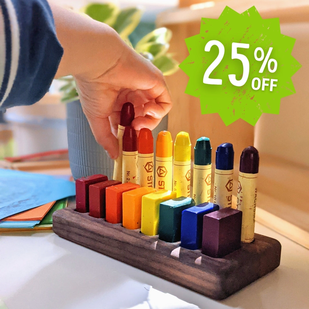 Colourful STOCKMAR crayons on a wooden stand with a hand reaching for one, promotional badge indicating 25% off.