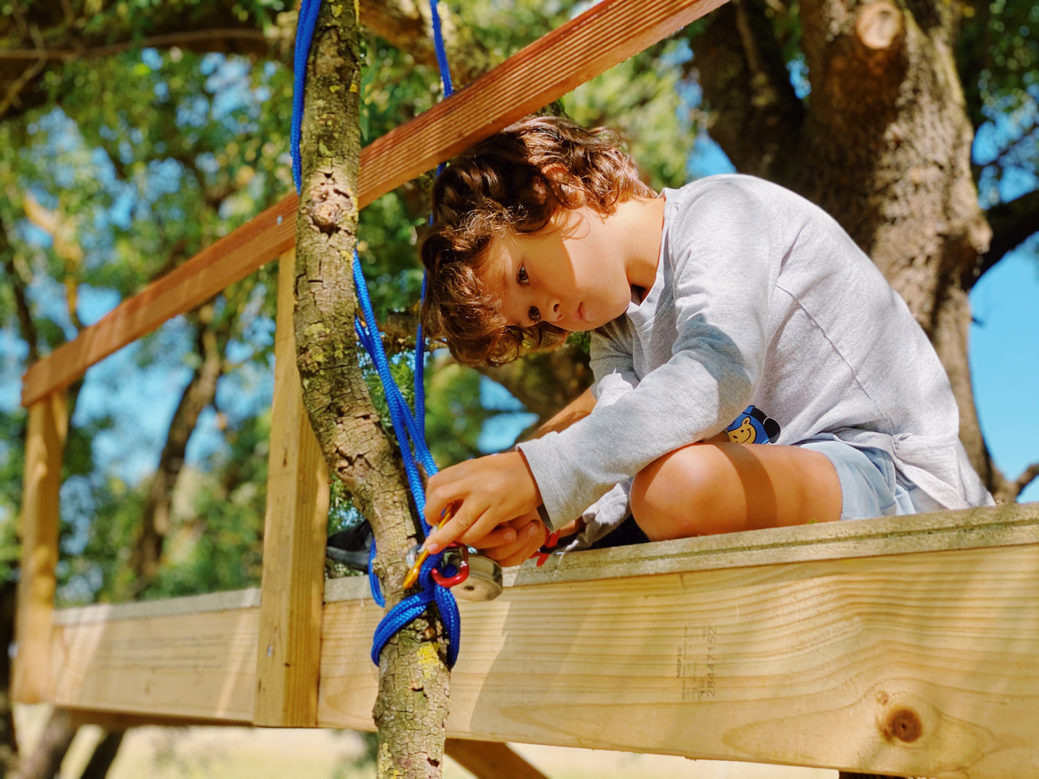 Child tying rope onto a tree branch using Kids at Work outdoor tools, pullys, clips, and skills