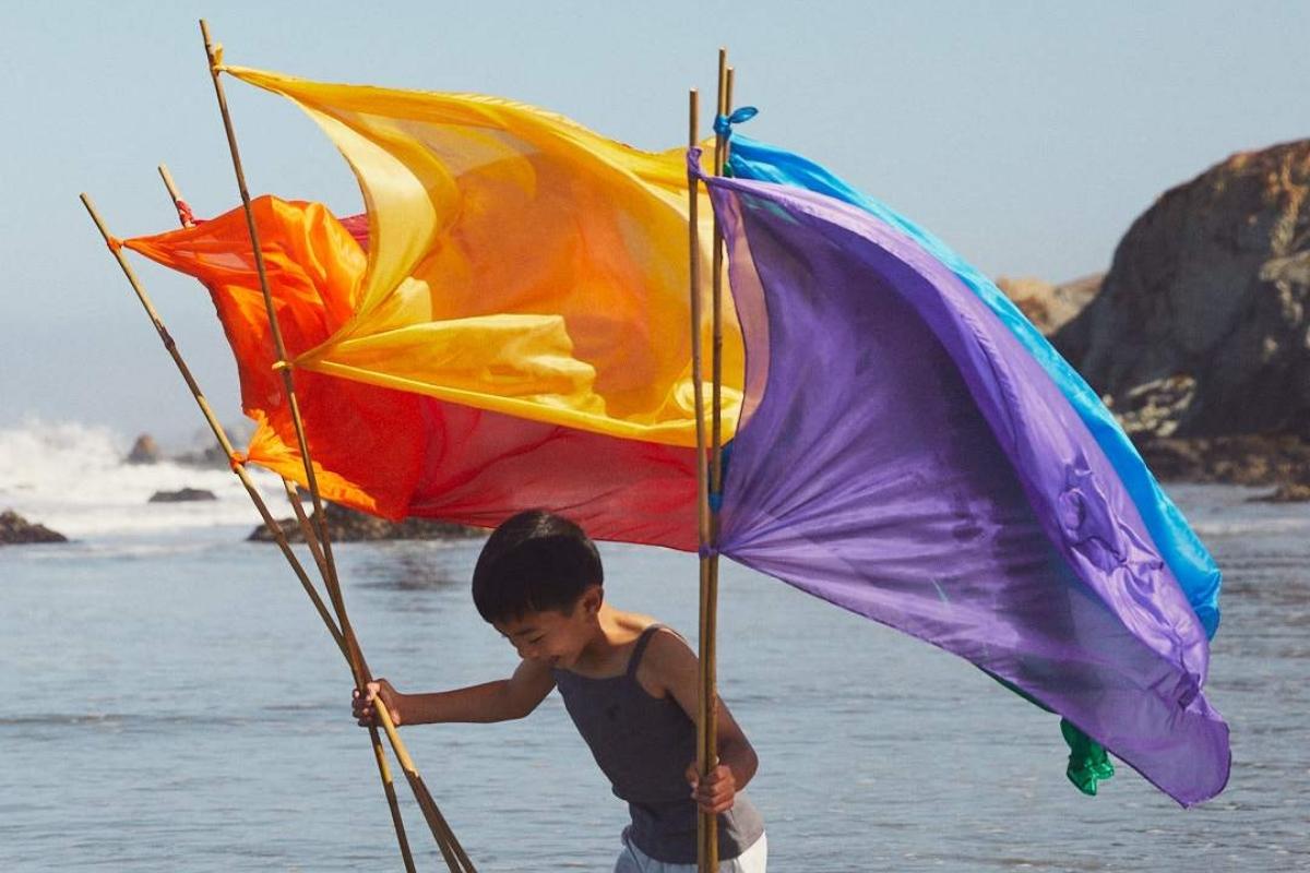 Child holding colorful Sarah's Silks playsilk flags by the seaside