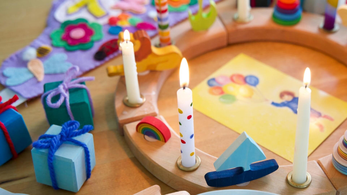Children's party table with Grimm's celebration ring, candles, toys, and colourful decorations on a wooden surface.