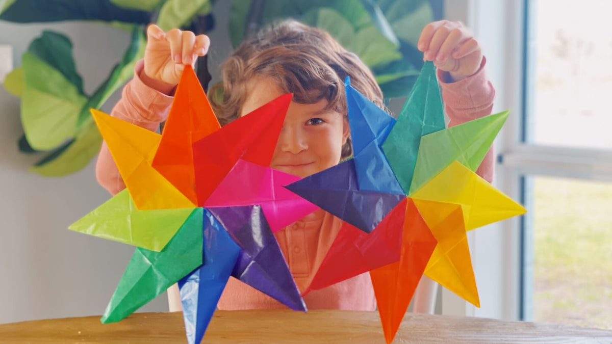 Child holding colourful origami stars in front of a window with greenery outside.