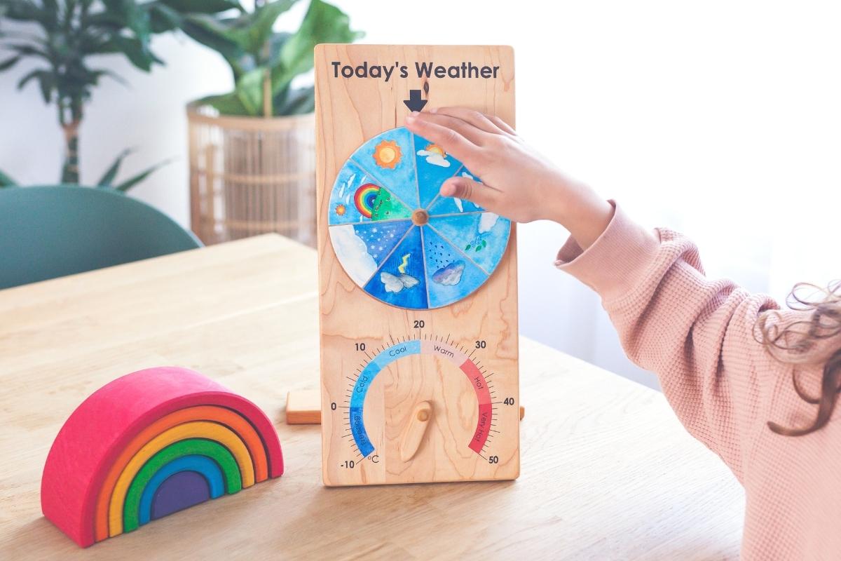 Child updating wooden From Jennifer weather chart alongside Grimm's rainbow as part of daily rhythm - Oskar's Wooden Ark