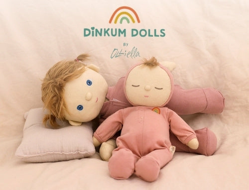 Two dolls on a pink surface with 'Dinkum Dolls' branding above.