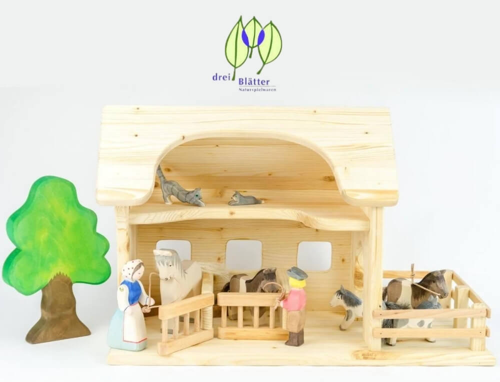 Drei Blatter lifestyle image with logo, featuring a two-story wooden toy stable with animal figures, a small painted green tree, and toy characters – Oskar's Wooden Ark