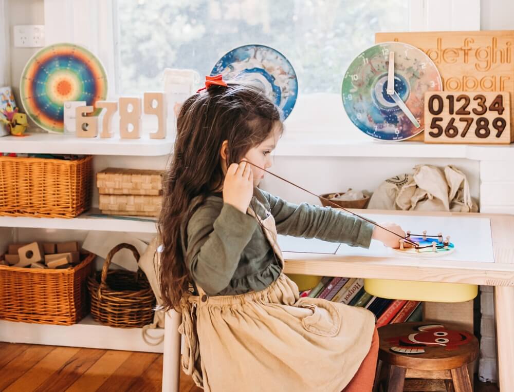 Girl child sitting at desk with multiplication number wheel, next to shelf of educational resources for home and schools from Oskar's Wooden Ark in Australia