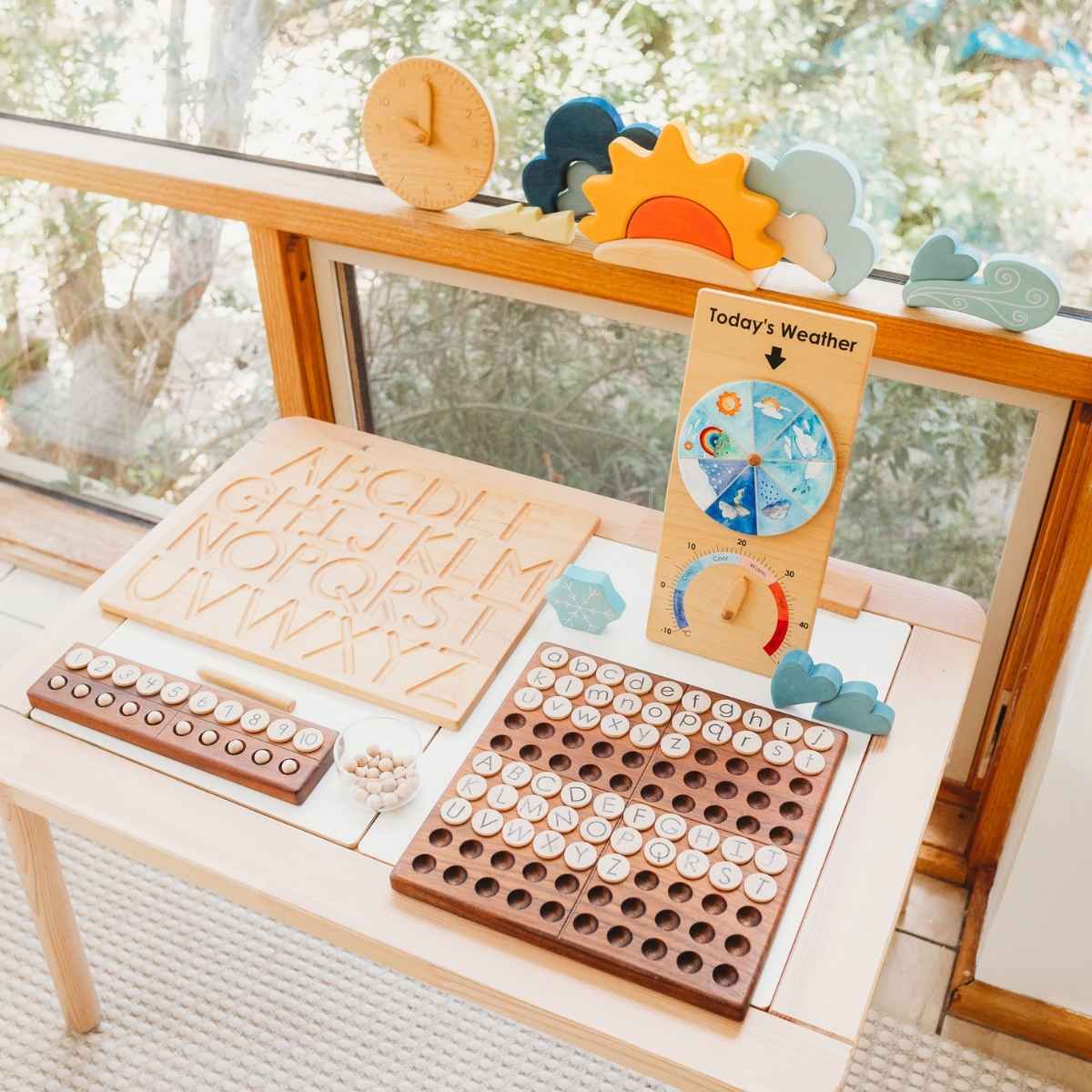 Classroom table with From Jennifer wooden educational resources including a teaching clock, alphabet tracing board, weather chart and hundred square - Oskar's Wooden Ark
