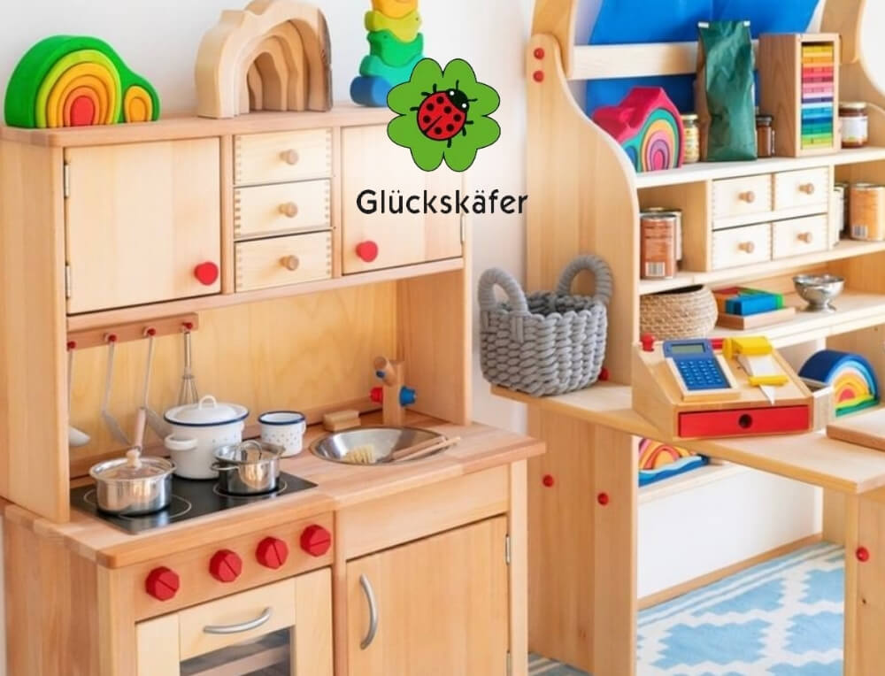 Gluckskafer Toys lifestyle image with logo, featuring a children's wooden play kitchen set with colourful toy accessories, shown in a bright playroom setting – Oskar's Wooden Ark