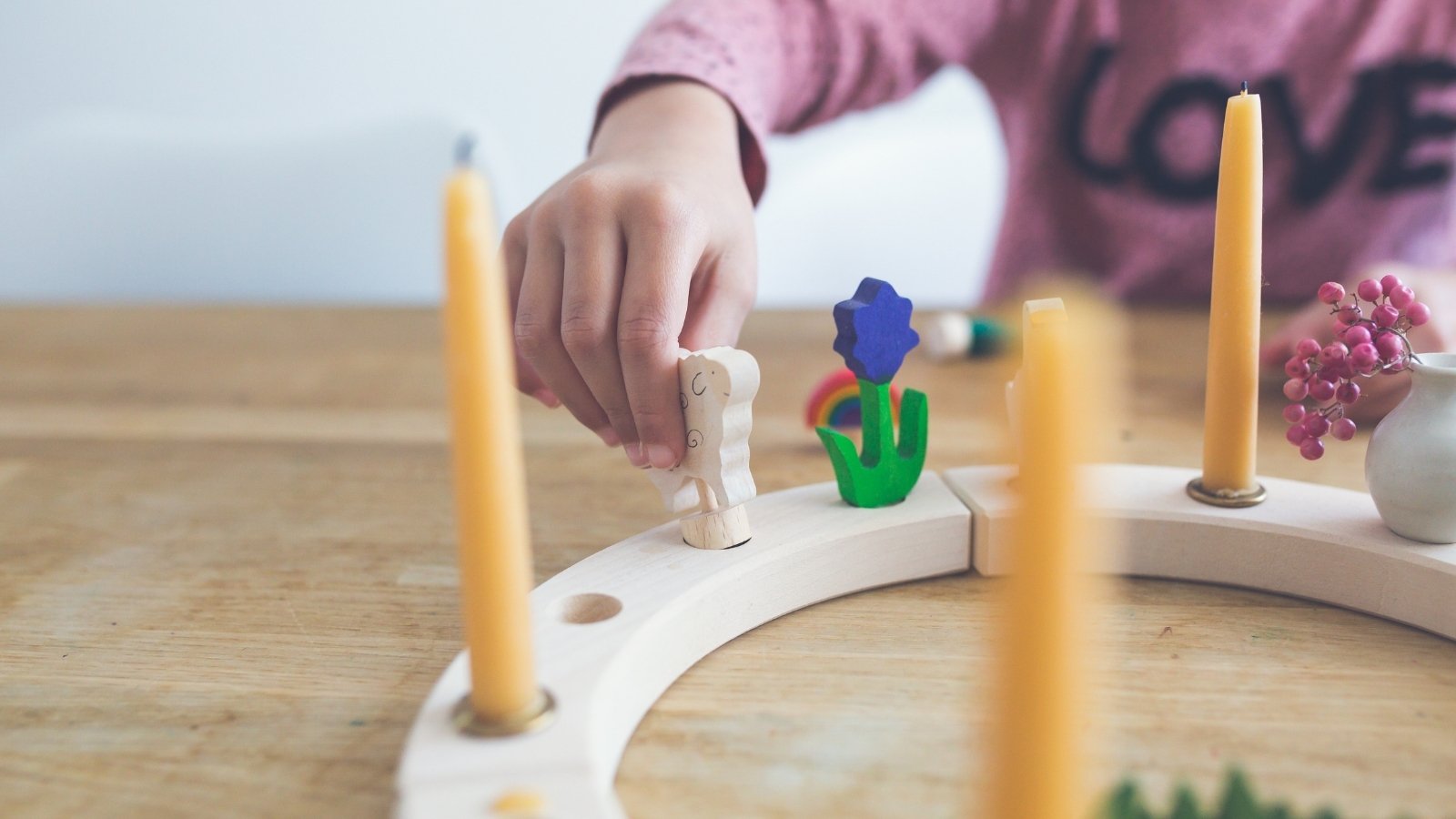 Child building a Grimm's Celebration Ring table centrepiece with candles and colourful celebration figures