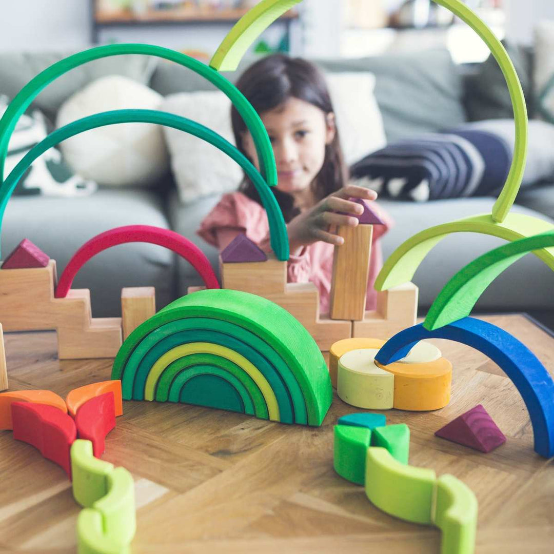 Child building an imaginative construction using Grimm's wooden toys and rainbow arches in a living room setting