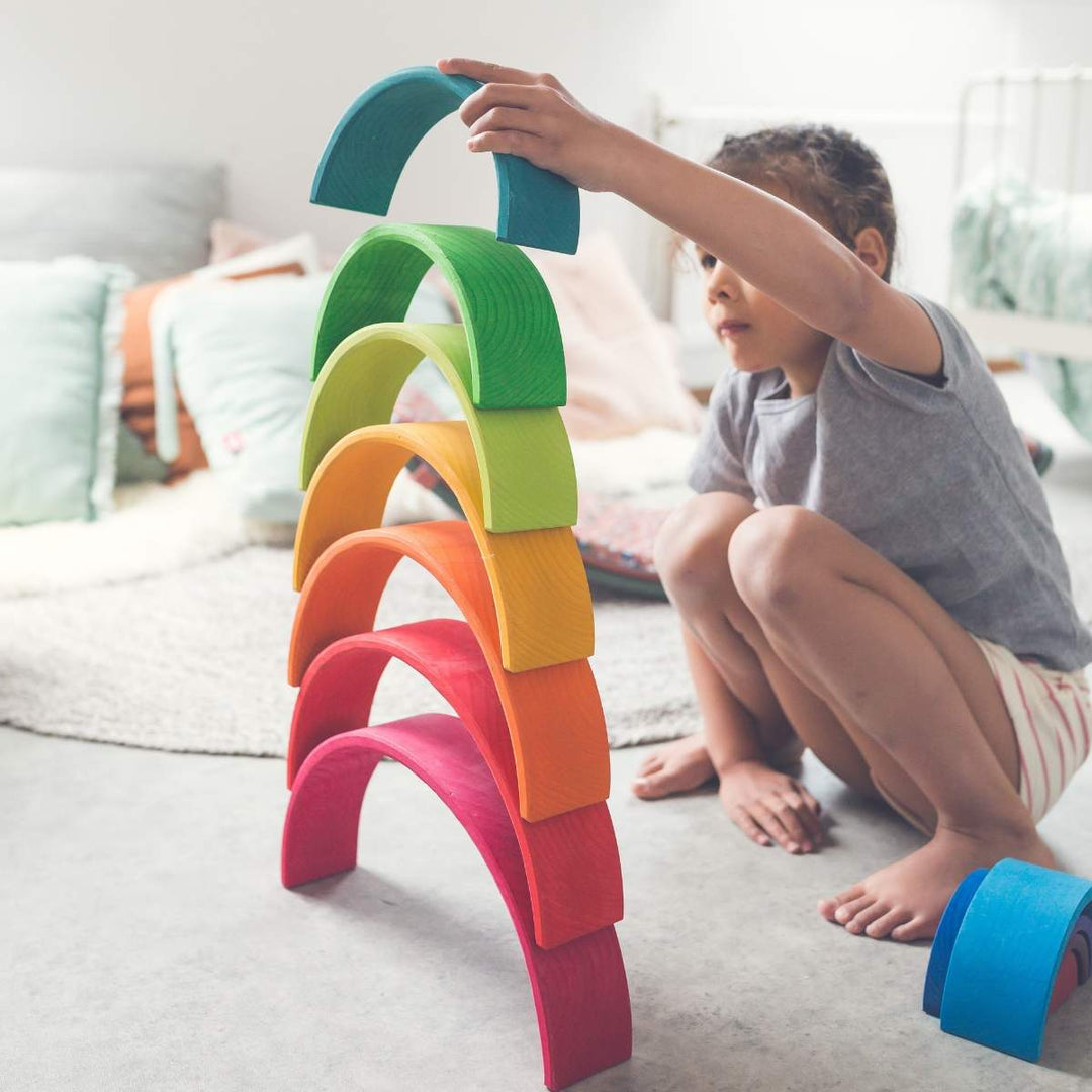 Child building a tower with colourful Grimm's Rainbow arches in a bedroom setting