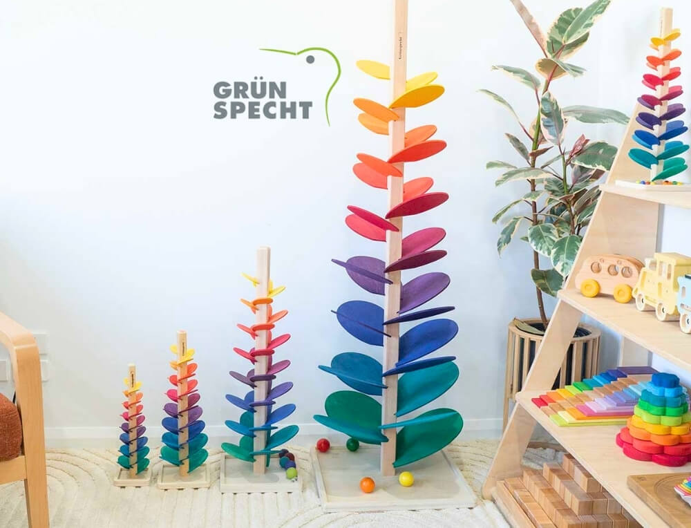 Grunspecht lifestyle image with logo, featuring four different sized wooden musical marble tree towers in a playroom setting - Oskar's Wooden Ark