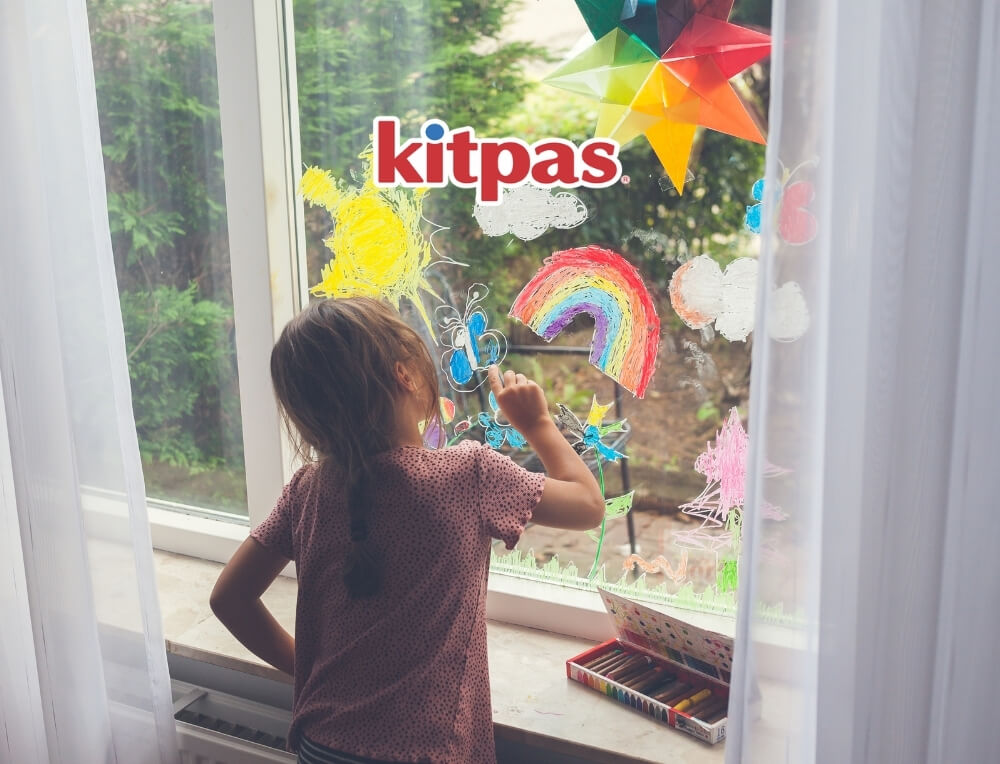 Kitpas Art lifestyle image with logo, featuring a child creating colourful drawings on the glass of a window, including a rainbow and butterflies, using Kitpas water-soluble crayons – Oskar's Wooden Ark