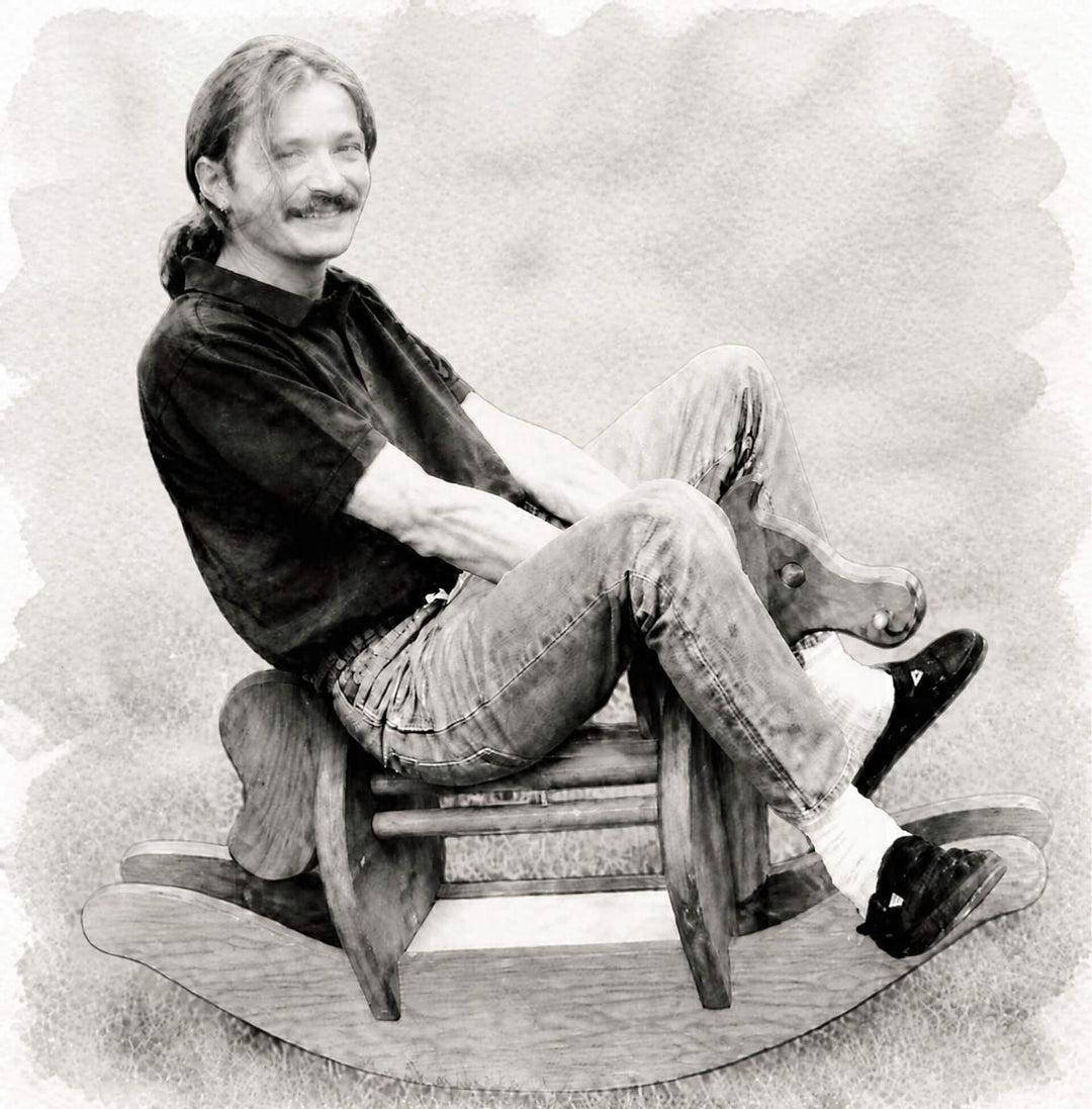 A black and white portrait-style photo of Klaus Mader sitting on a wooden rocking horse. The image has a textured, sketched or painted border effect around the edges.