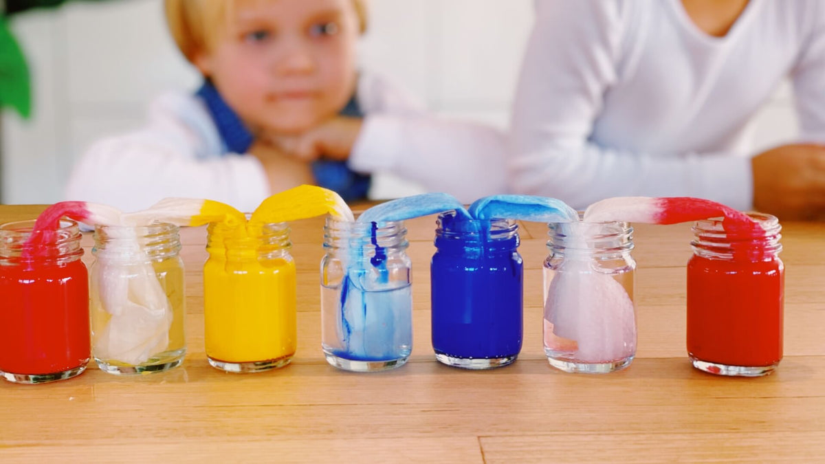 Colourful paint bottles on a table as part of a science experiment with children in the background