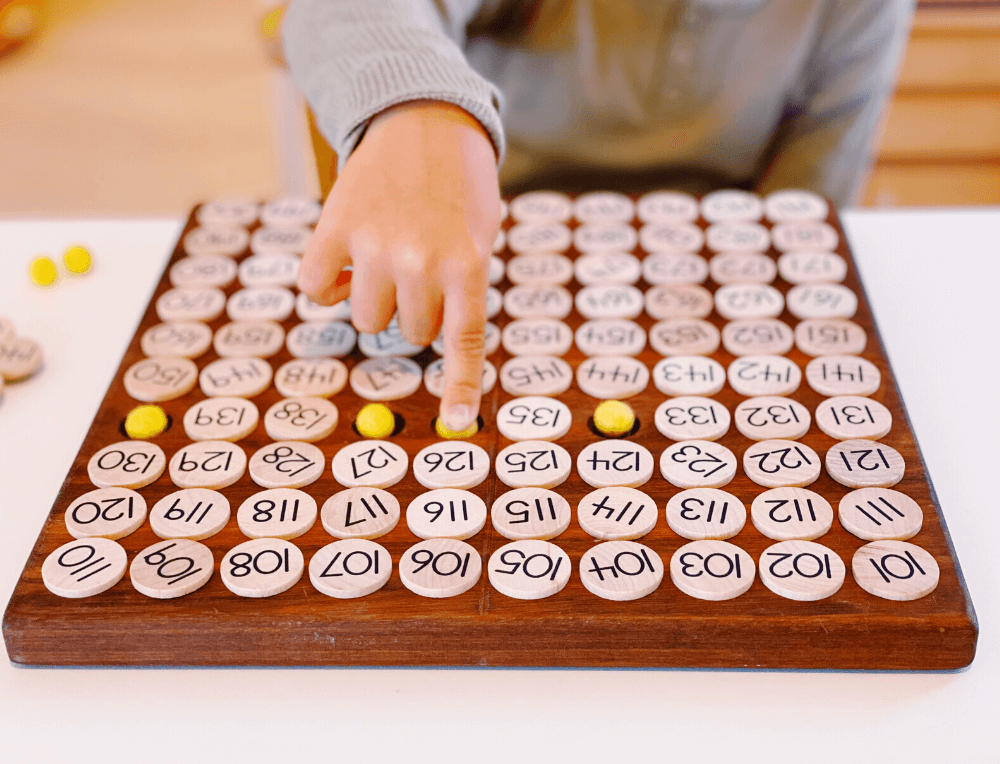 Child using the Treasures From Jennifer multiplication 100 board with numbers and beads for learning maths skills, at Oskar's Wooden Ark in Australia