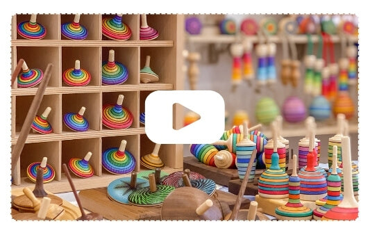 Colourful Mader spinning tops and wooden toys on shelves with a play button overlay