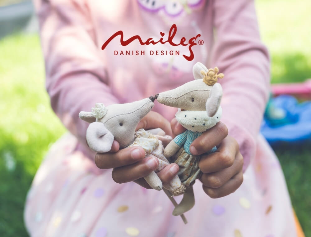 Maileg lifestyle image with logo, featuring a child holding two small fabric Maileg mice animals outdoors – Oskar's Wooden Ark
