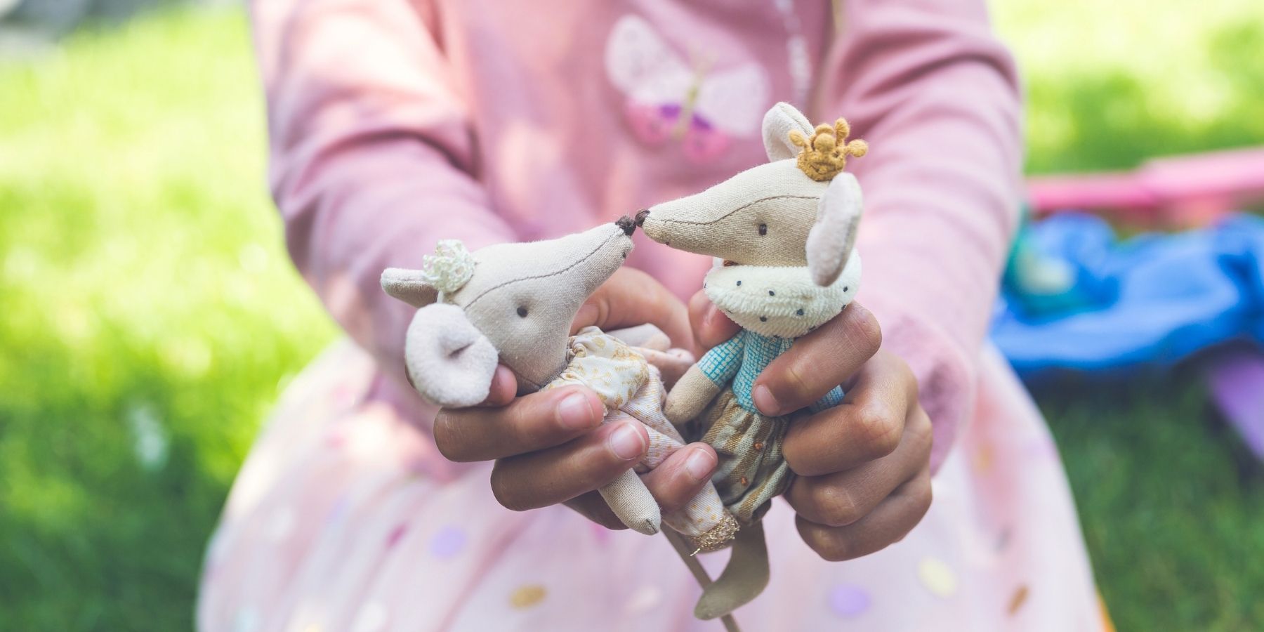Two small Maileg mice animal figurines held by a child in a park setting