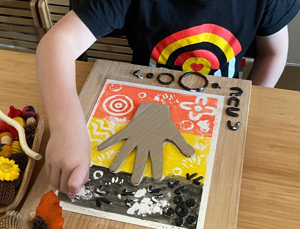 Child painting over beeswax symbols with Aboriginal flag colours