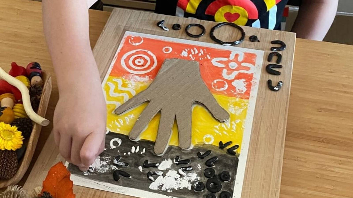Child painting over beeswax symbols with Aboriginal flag colours for NAIDOC Week