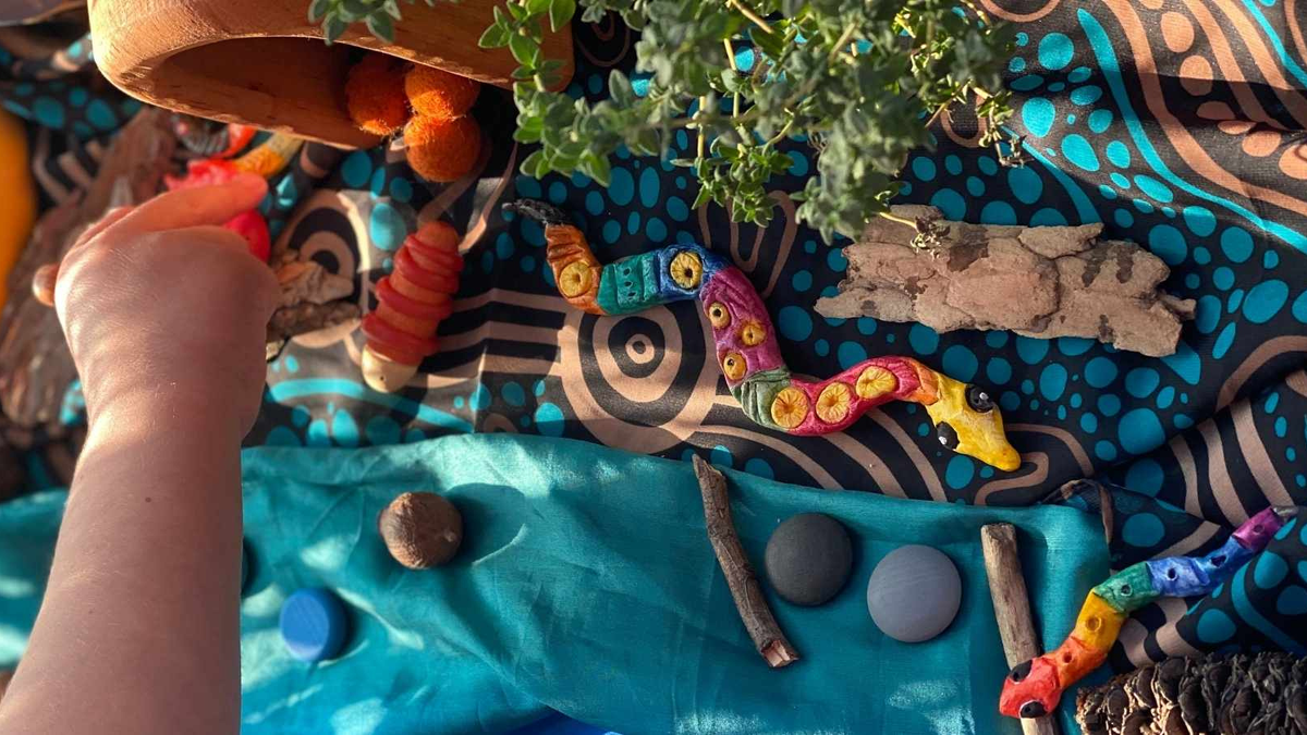 A child playing with a finished serpent-themed nature artwork for NAIDOC Week