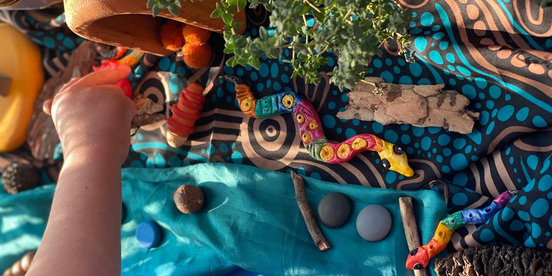 A child playing with a finished serpent-themed nature artwork for NAIDOC Week