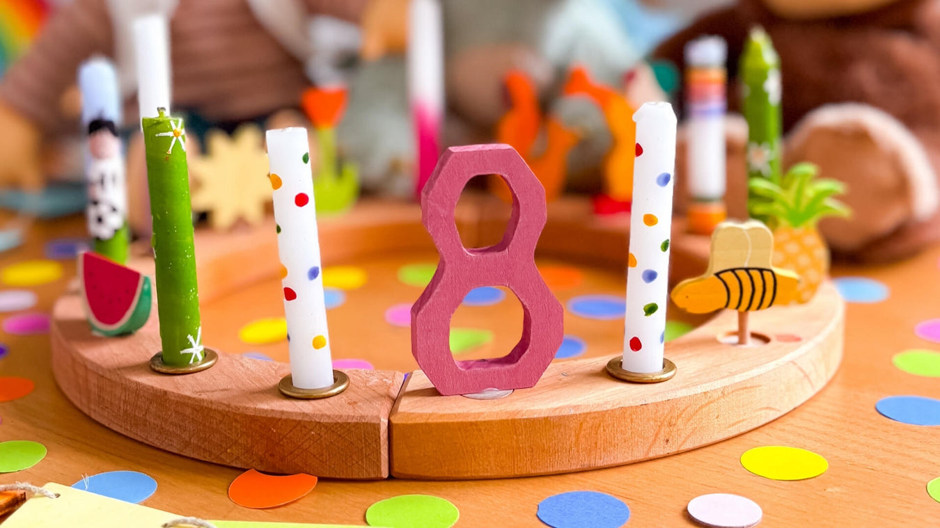 Wooden birthday celebration ring with candles and number '8' on a colourful table.