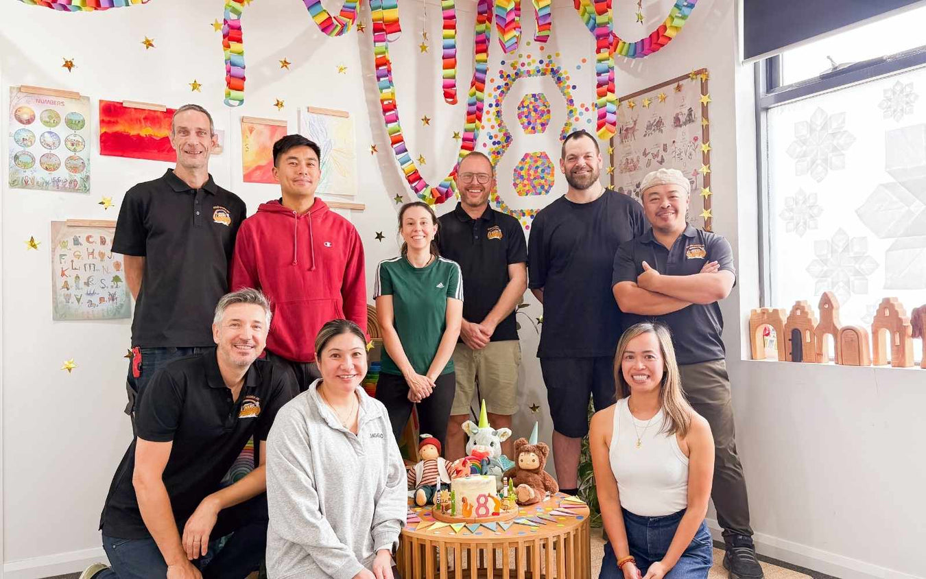 Oskar's Wooden Ark Team posing for a photo in a room with colourful decorations and a birthday cake.
