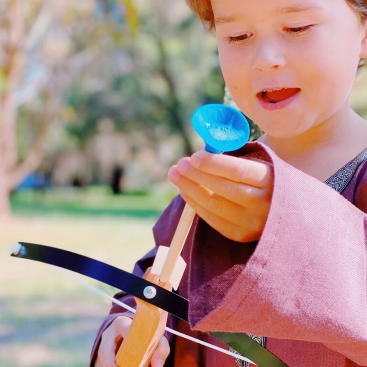 Boy dressed as a knight aiming a VAH wooden crossbow outdoors