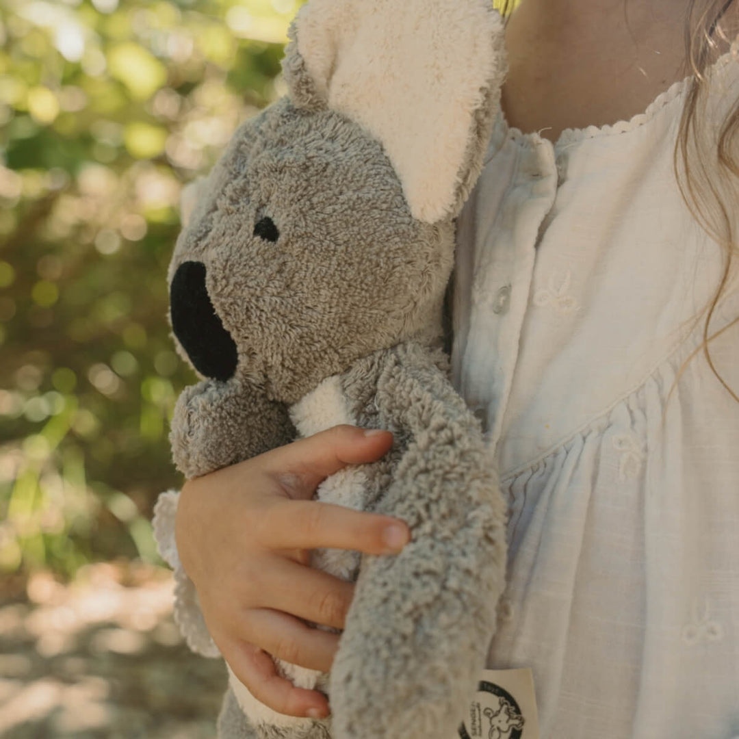 A child in a white dress holds a limited edition SENGER koala toy outdoors with a soft, blurred green and yellow background  - Oskar's Wooden Ark Australia