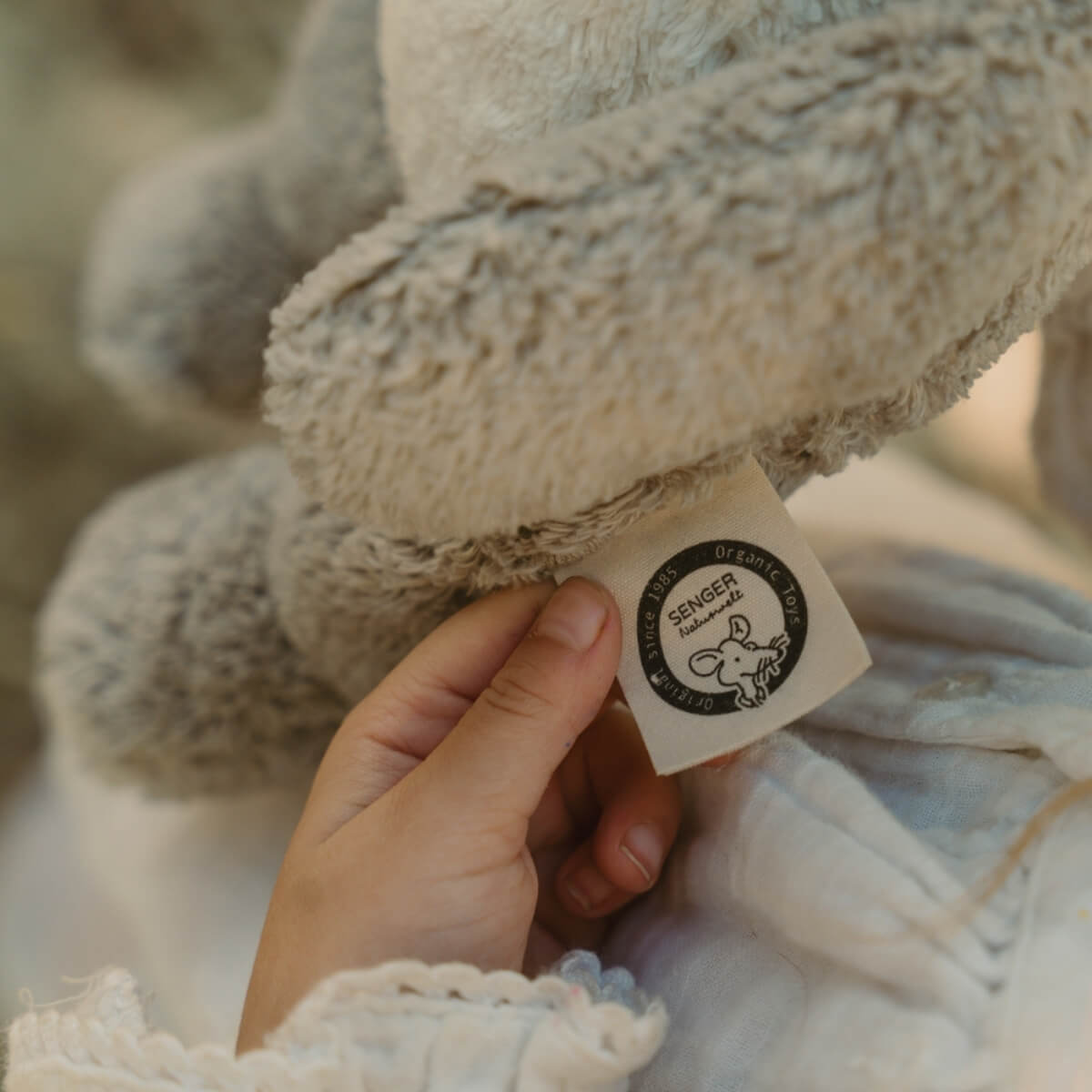 A close-up of a person's hand holding a small fabric tag attached to a soft limited edition SENGER plush toy. The tag reads 'SENGER NATURWELT' in a circular black-and-white logo  - Oskar's Wooden Ark Australia