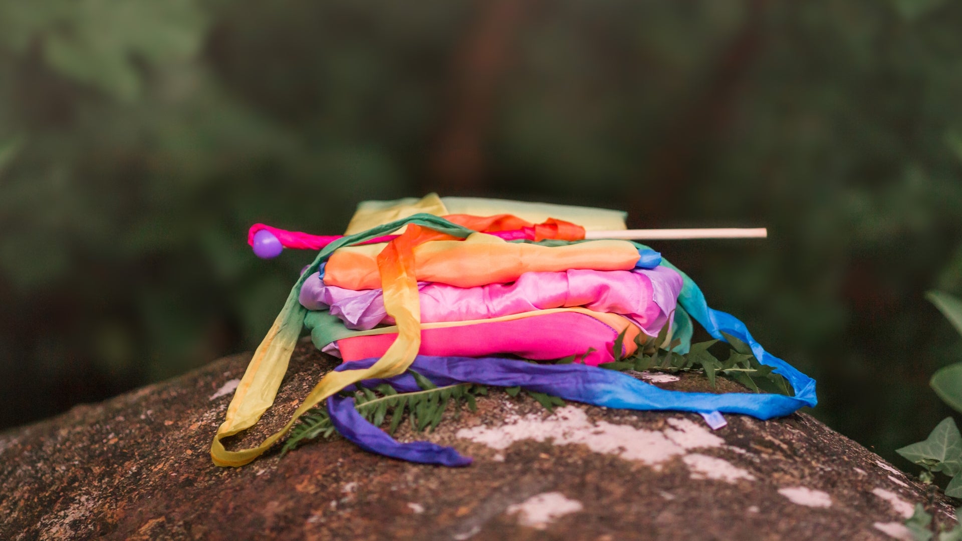 Stack of colourful Sarah's Silks costumes and streamers on a wooden surface with a blurred natural background