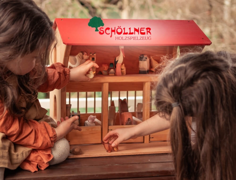 Schollner lifestyle image with logo, featuring rtwo children playing with a wooden Schöllner barn, with wooden animal figures – Oskar's Wooden Ark