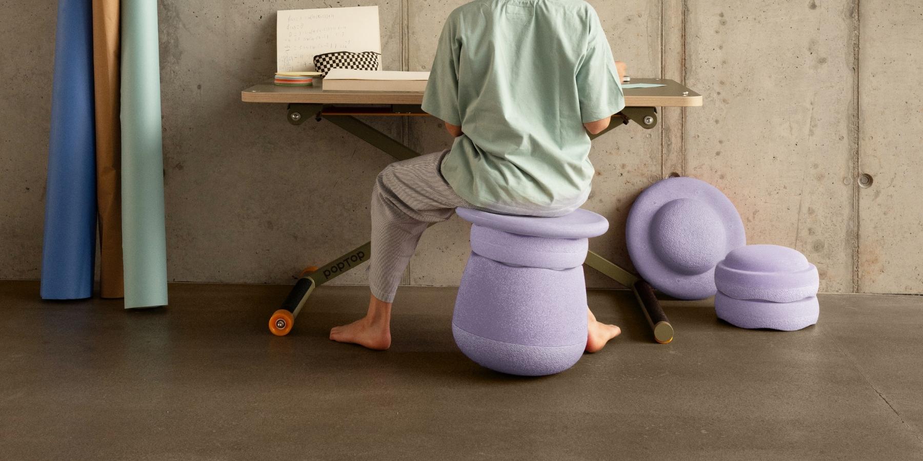 Child sitting on a Stapelstein Dynamic Set in light violet while working at a desk, with other Stapelstein stepping stones stacked on the floor next to him
