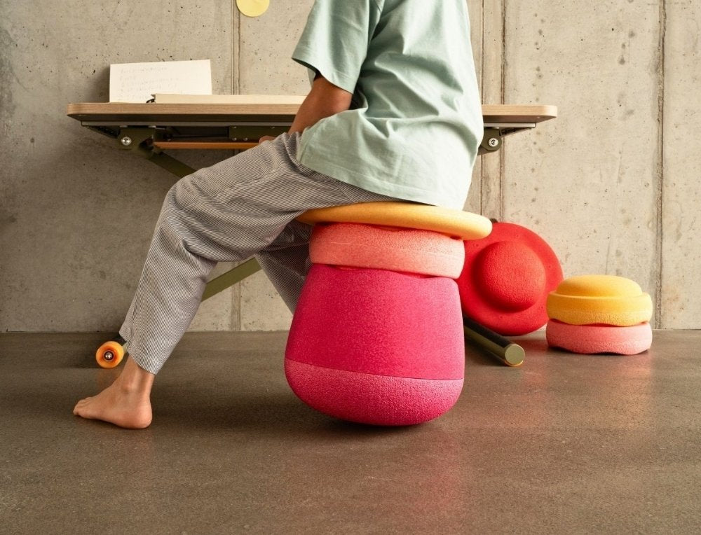 Child sitting on colorful Stapelstein Dynamic seating in a room with a concrete wall.